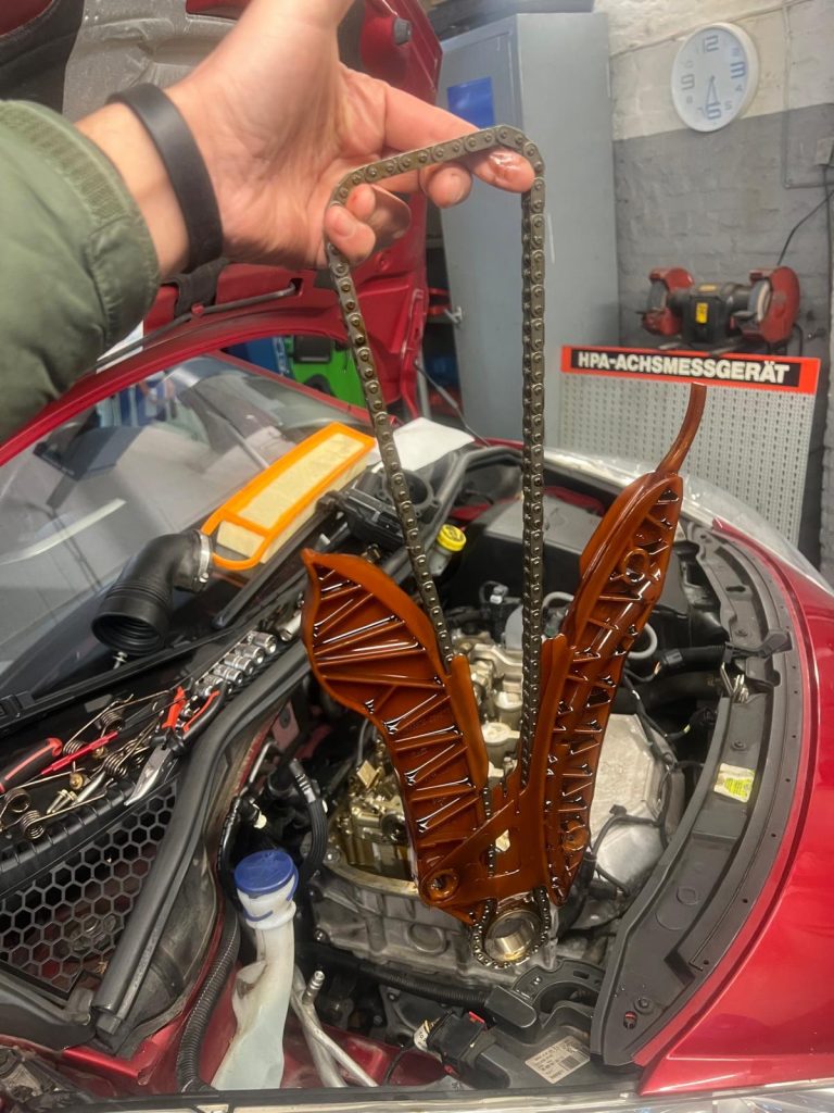 Ausgebaute Steuerkette mit Gleitschiene über dem geöffneten Motorraum